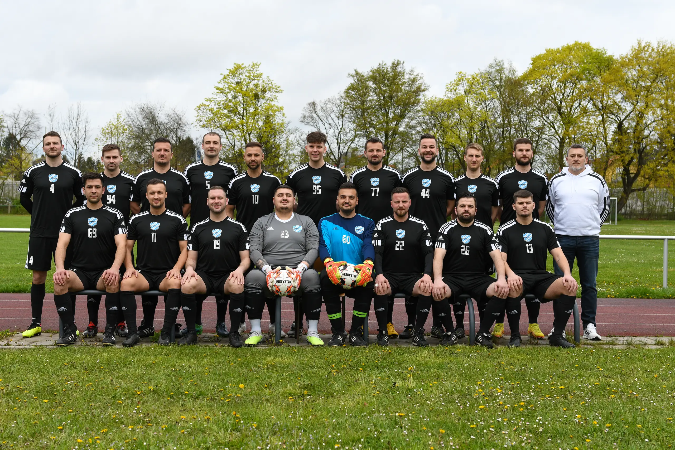 Mannschaftsfoto der Münchner Kickers 2015: Spieler in schwarzen Trikots und Betreuer auf dem Sportplatz